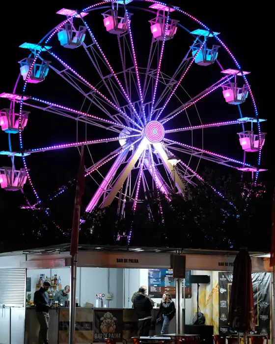 Roda gigante iluminada, à noite, no recinto